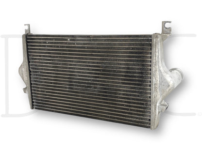 Used OE 99-02 Ford F250 F350 7.3 7.3L Powerstroke Diesel Intercooler Charge Air Cooler with light wear, compatible with 1999-2002 Ford Excursion, F-250, F-350, F-450, and F-550 trucks, showing the cooling fins and inlet/outlet pipes.