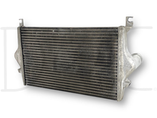 Used OE 99-02 Ford F250 F350 7.3 7.3L Powerstroke Diesel Intercooler Charge Air Cooler with light wear, compatible with 1999-2002 Ford Excursion, F-250, F-350, F-450, and F-550 trucks, showing the cooling fins and inlet/outlet pipes.