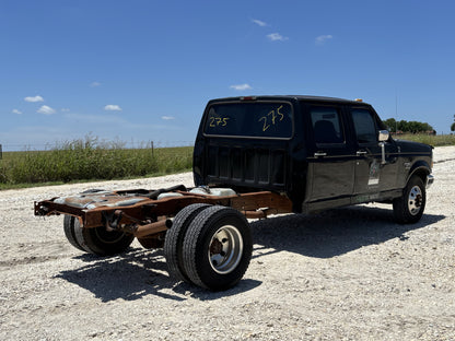 92-97 Ford F250 F350 Hood Ua Black installed on a partially disassembled black Ford truck cab with dual rear wheels and rusted chassis on a gravel lot under a clear sky.
